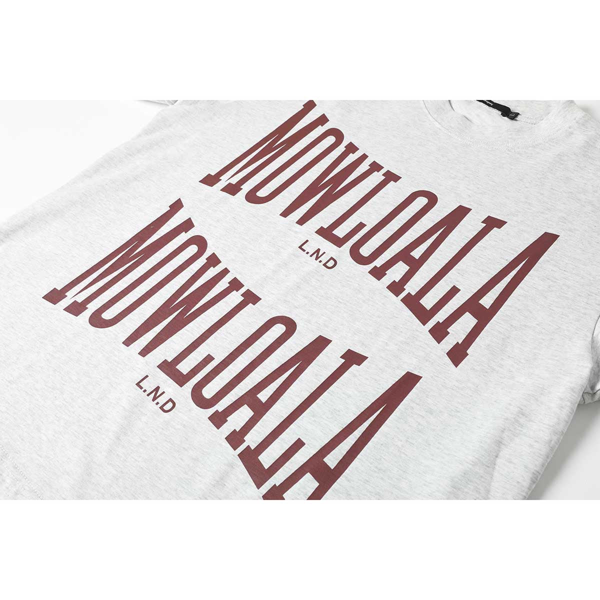 Angled close-up of a light gray T-shirt with oversized burgundy lettering printed across the chest.