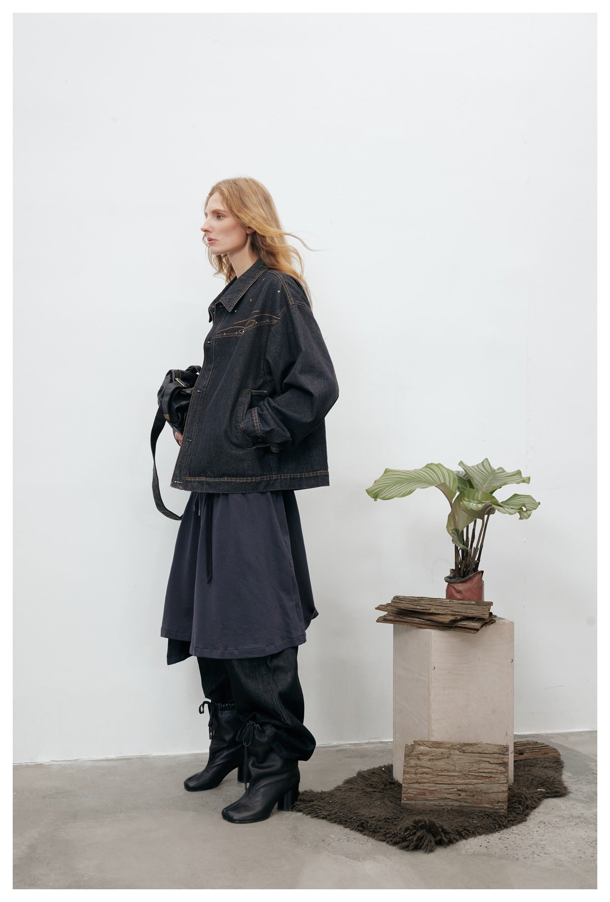 Model wearing an oversized charcoal denim jacket with bronze stitching and star embellishments, layered over dark clothing.