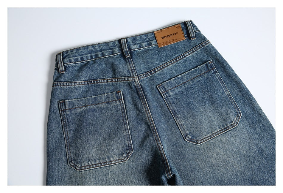 Flat lay of the upper back of faded blue jeans, showing two rear pockets, belt loops, and a leather waistband patch.