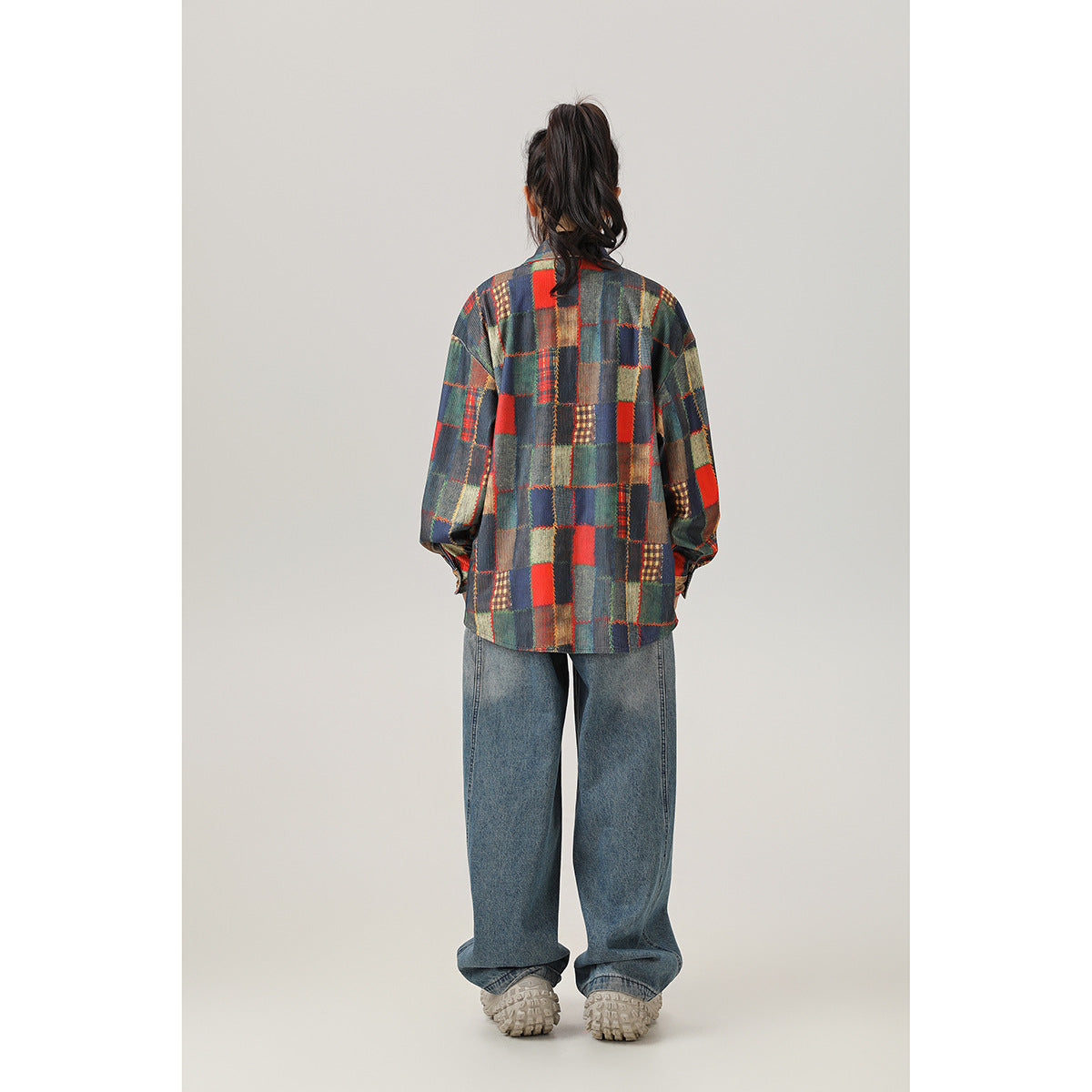 Full-length back view of a model wearing a multicolor patchwork plaid shirt and wide-leg jeans.