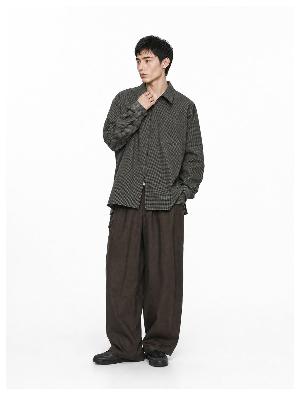 Model wearing an open-front black check zip shirt jacket with chest pocket and wide brown pants