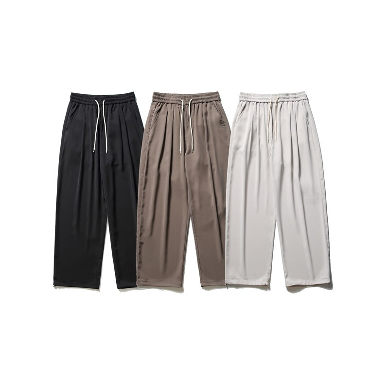 Three pairs of loose drawstring trousers shown together in black, brown, and pale gray.