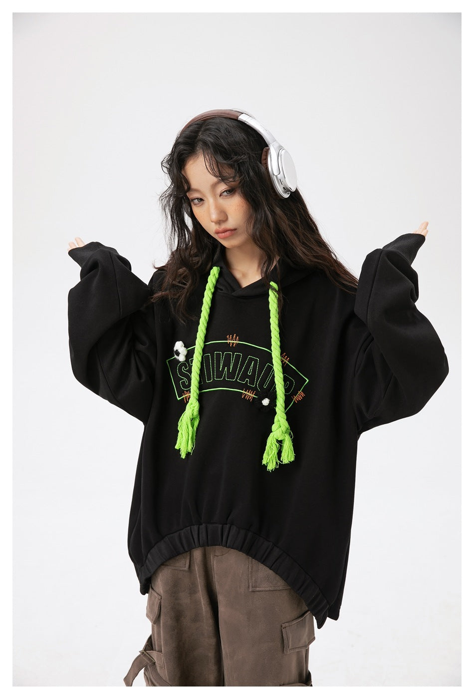 Model wearing a black hoodie with neon green braided drawstrings, outlined chest lettering and small decorative details.