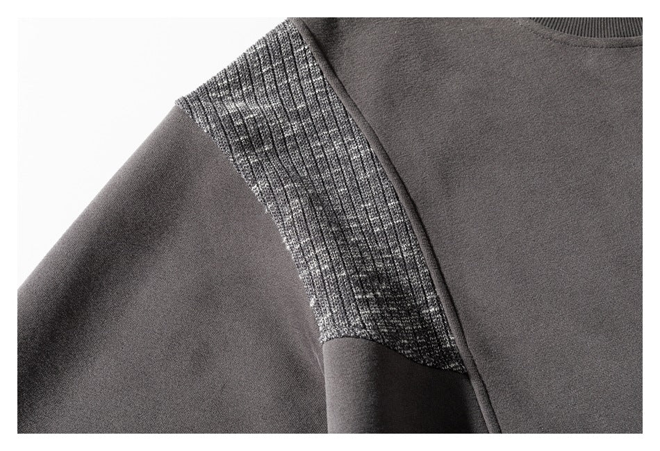 Close-up of a charcoal sweatshirt's marled rib-knit shoulder panel beside the smooth body and sleeve.