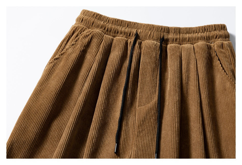 Close-up of the brown corduroy trousers' elastic waistband, front pleats, and black drawstrings.
