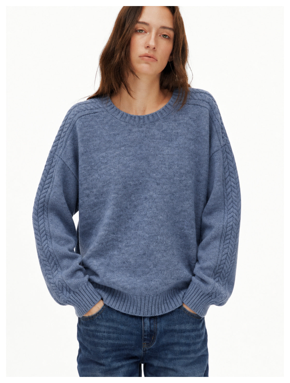 Closer view of a blue-gray crewneck sweater on a model, showing cable-knit sleeves and ribbed trim.