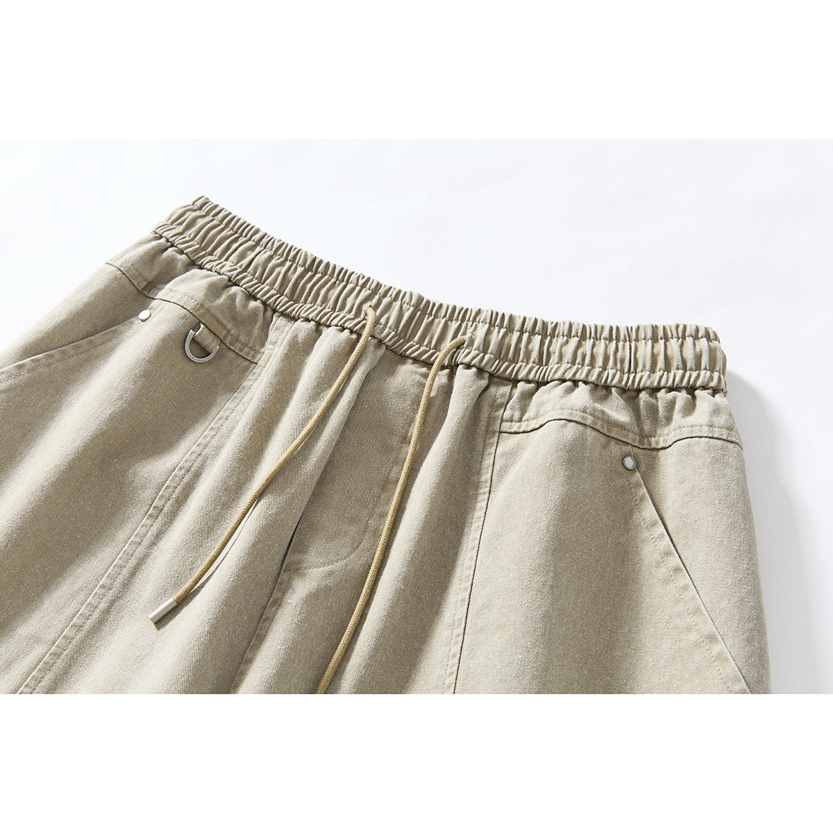 Close-up of beige wide-leg shorts showing the elastic waistband, drawstrings, front pockets and metal details.