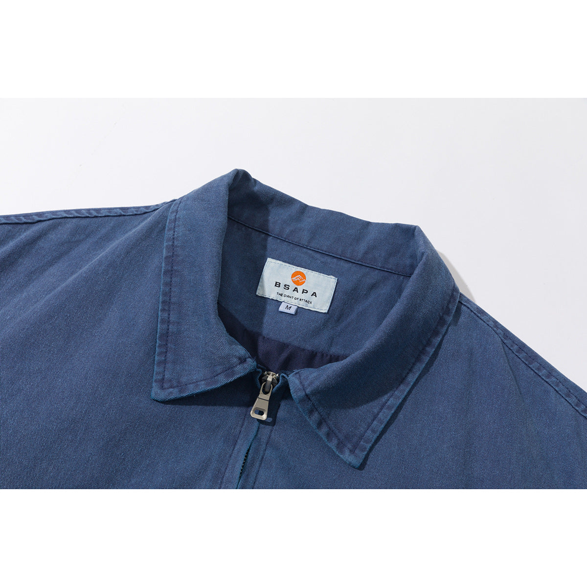 Close-up of a blue jacket's pointed collar, front zipper, and sewn neck label.
