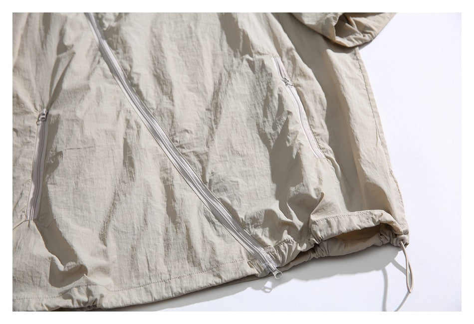 Flat-lay view of part of a beige jacket showing its diagonal front zipper, zip pockets, and adjustable hem.