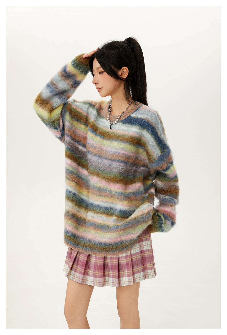 Side view of a model wearing an oversized multicolored striped sweater and pink plaid pleated skirt.