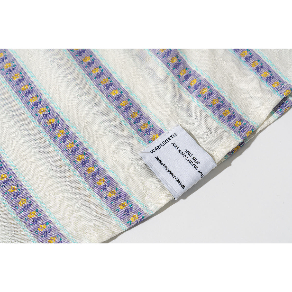 Close-up of a sewn label and hem on an ivory shirt with purple floral stripes and turquoise edging.