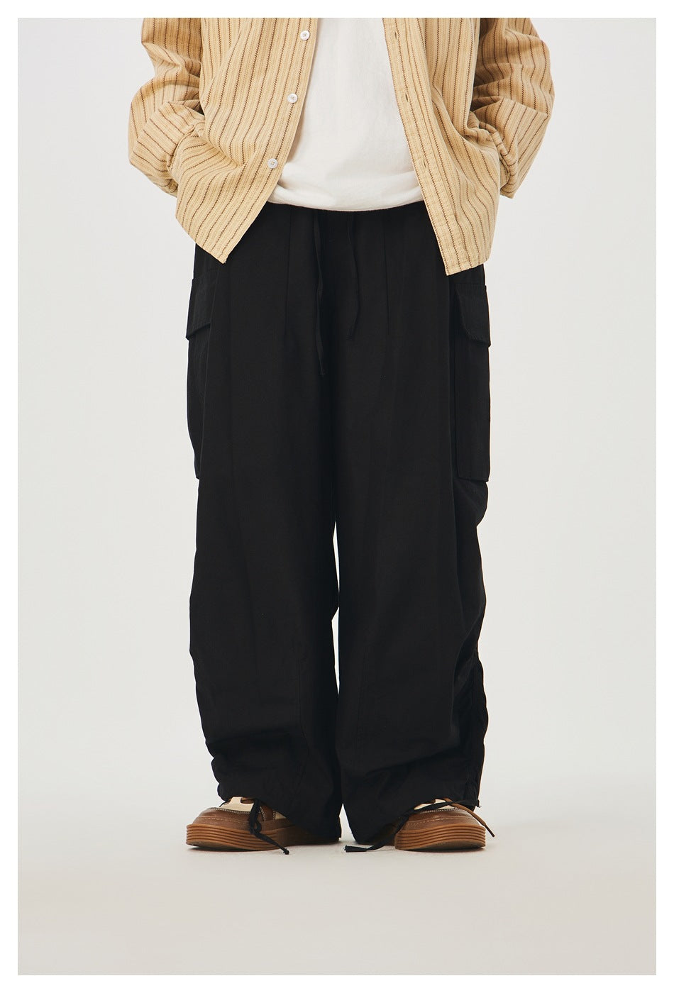 Cropped front view of a model wearing loose black cargo pants with side pockets and adjustable gathered hems.