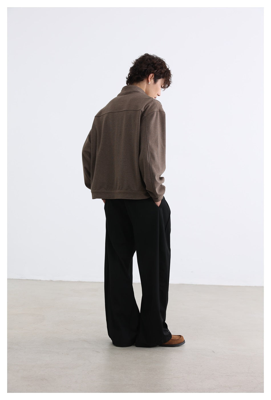 Rear three-quarter view of a model wearing a brown jacket with a horizontal back yoke and straight hem.