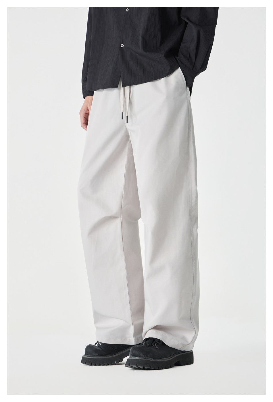 Cropped front view of a model wearing light gray wide-leg drawstring pants with a black shirt and shoes.