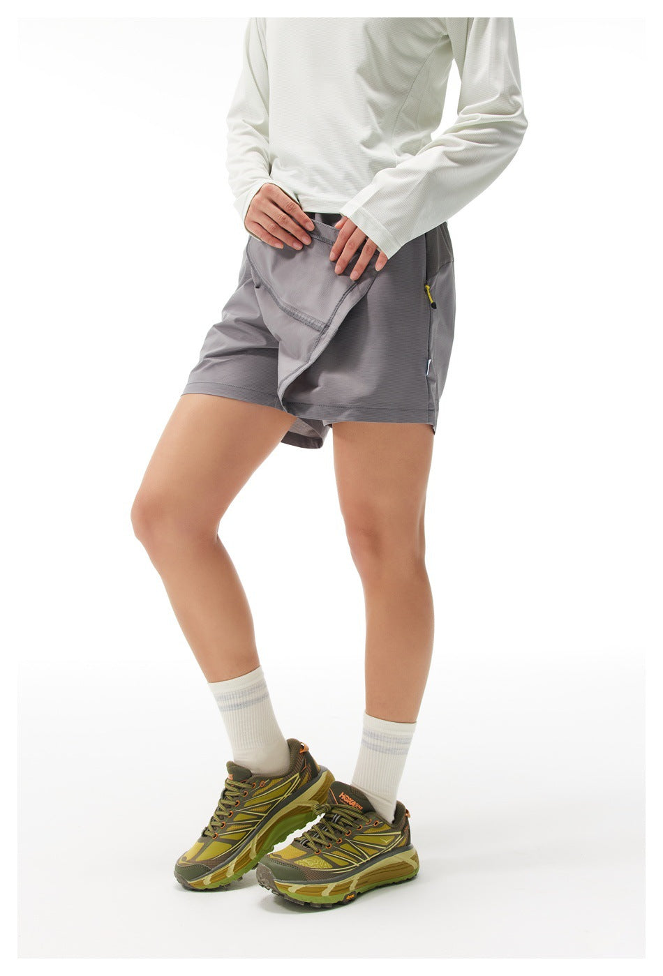 Model lifts the front flap of a gray athletic skort to show the shorts underneath and a zippered side pocket.