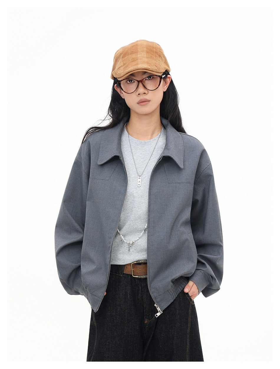 Model wearing gray collared jacket open over a light gray tee with dark jeans and a tan cap