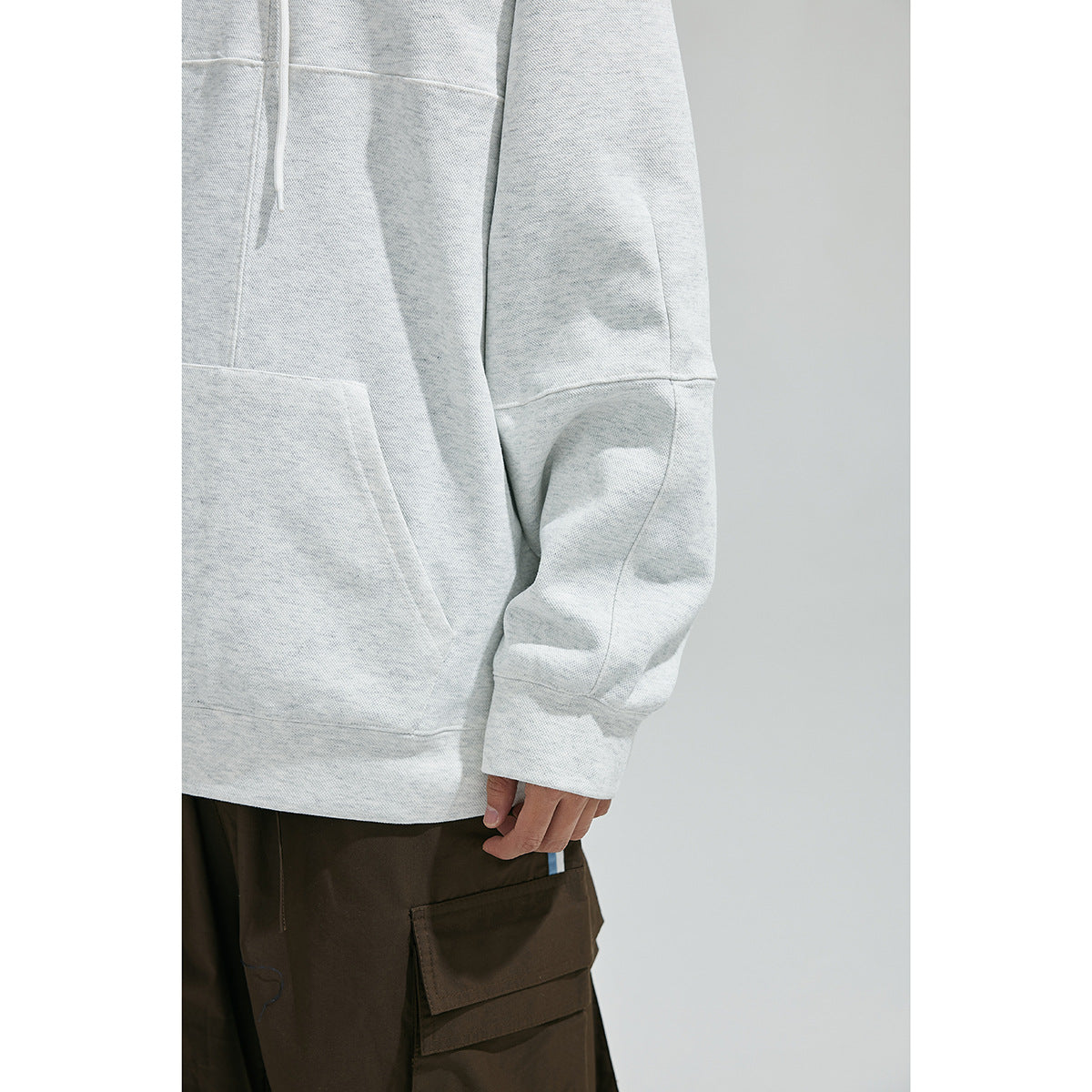 Close-up of the light gray sweatshirt's kangaroo pocket, long sleeve with panel seams, and ribbed cuff.