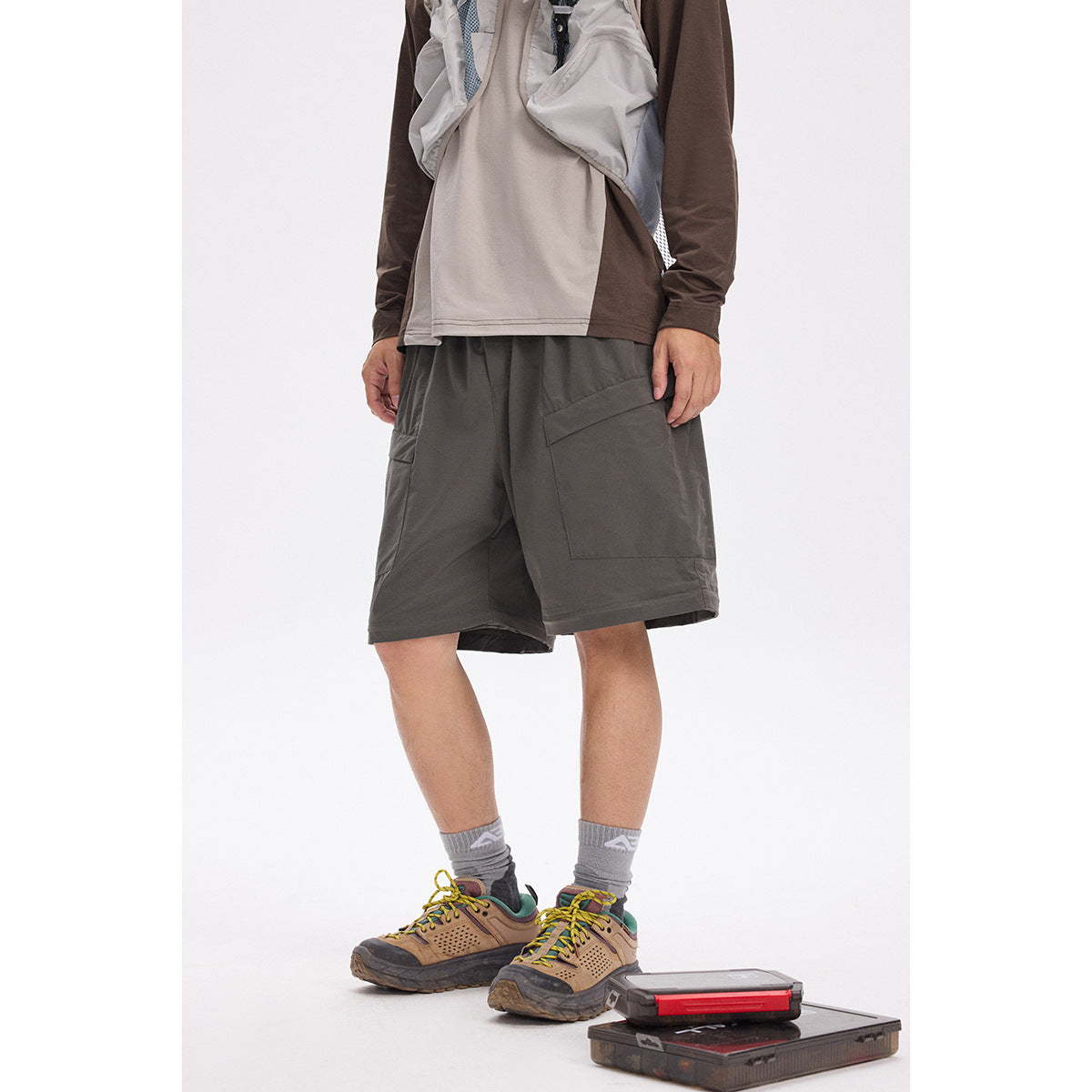 Model wearing dark charcoal cargo shorts with large thigh pockets and a layered, below-knee-length cut.