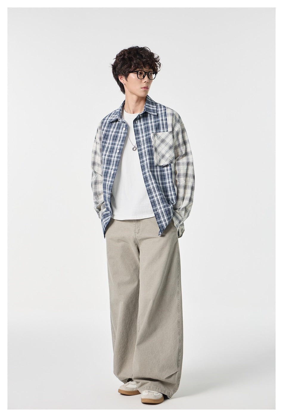 Model wearing an open navy, gray and white patchwork plaid shirt over a white tee and loose gray trousers.