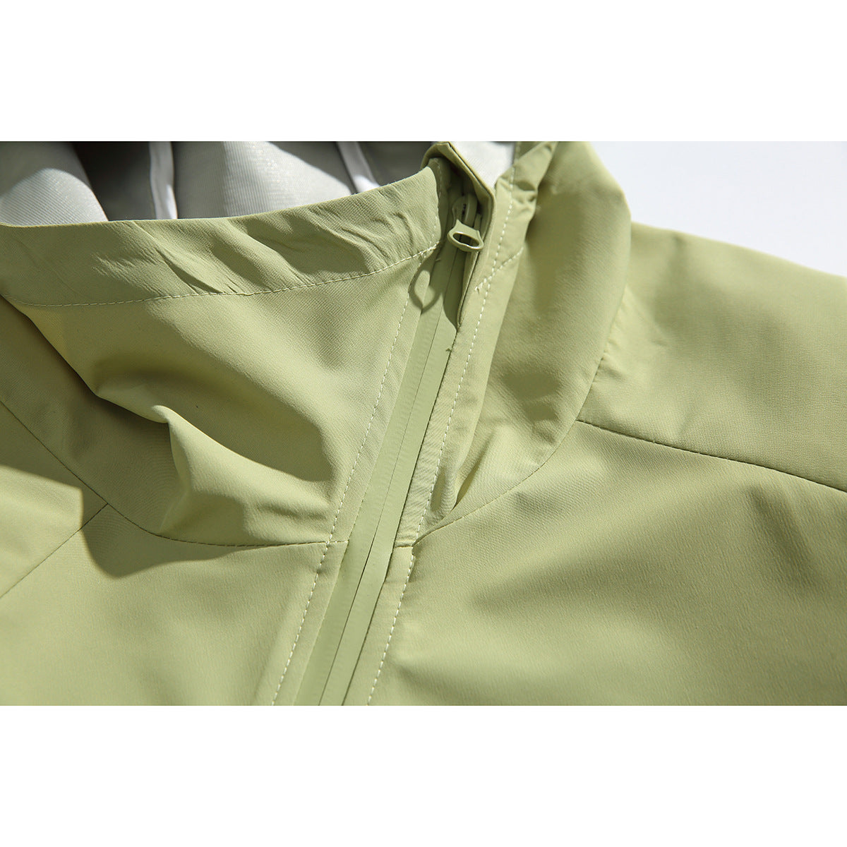 Close-up of a pale green hooded jacket showing the collar, central zipper and stitched panels.