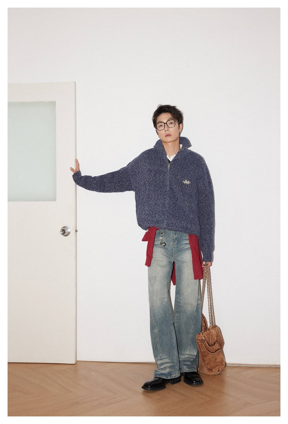 Model wearing a navy textured zip-up cardigan with a raised collar, wide faded jeans and a red layer tied at the waist.