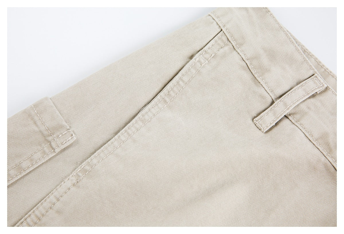 Close-up of light beige trousers showing a belt loop, waistband seam, and front pocket stitching.