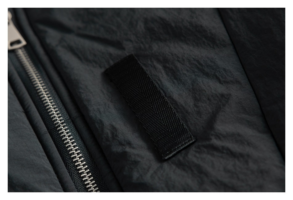 Close-up of a black jacket's silver zipper beside a small rectangular black fabric tab.