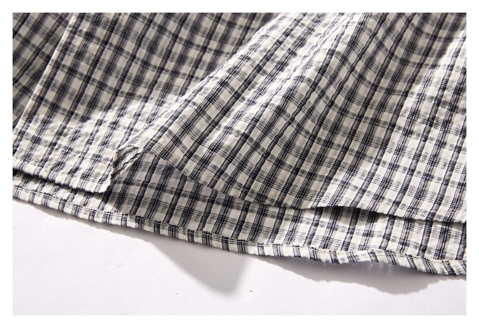 Close-up of the curved hem and side seam of a cream shirt with black and gray plaid.