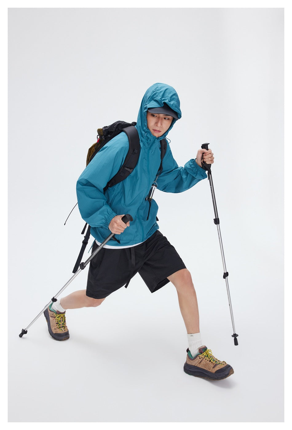 Person wearing a teal hooded zip jacket and black shorts while hiking with trekking poles and a backpack.