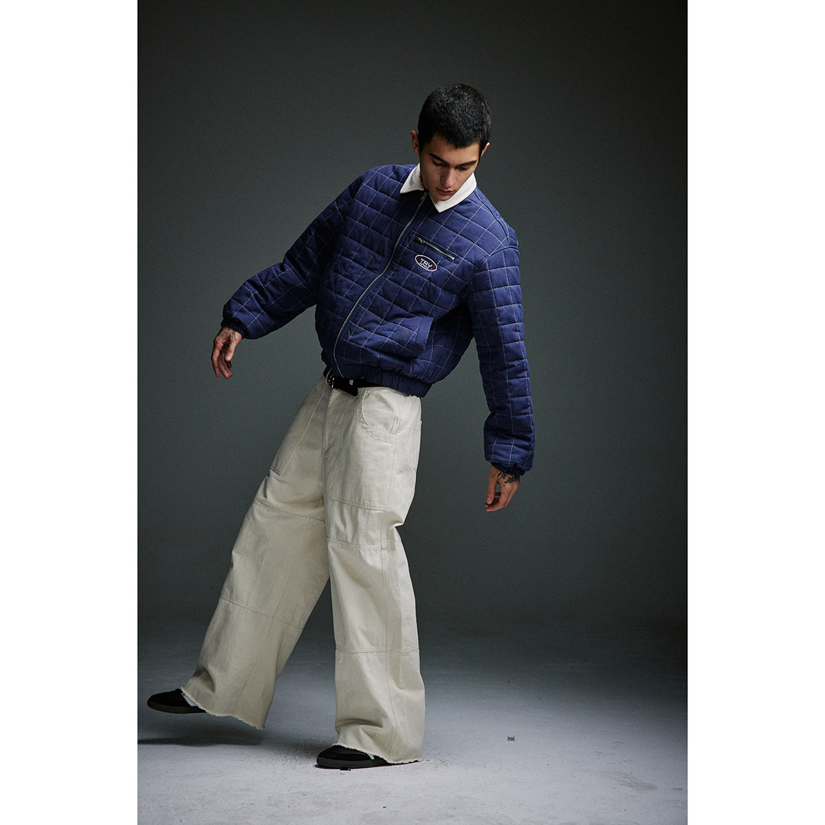 Full-length model wearing a navy grid-quilted jacket with a cream collar and wide cream trousers.