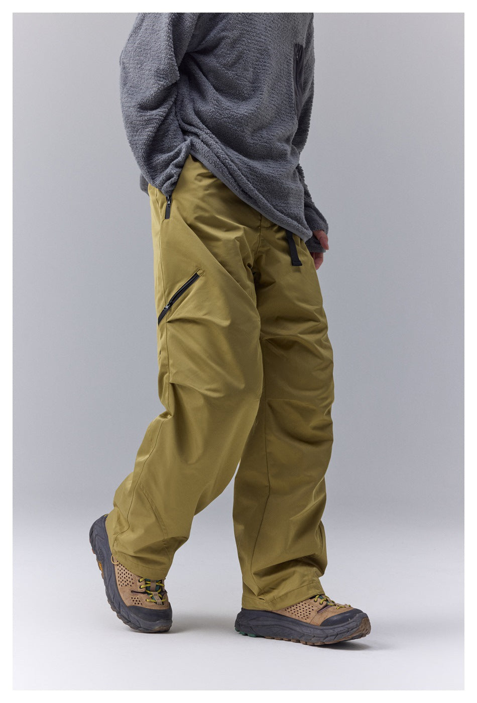 Side-angle view of olive-yellow pants showing a black zip pocket on the thigh.