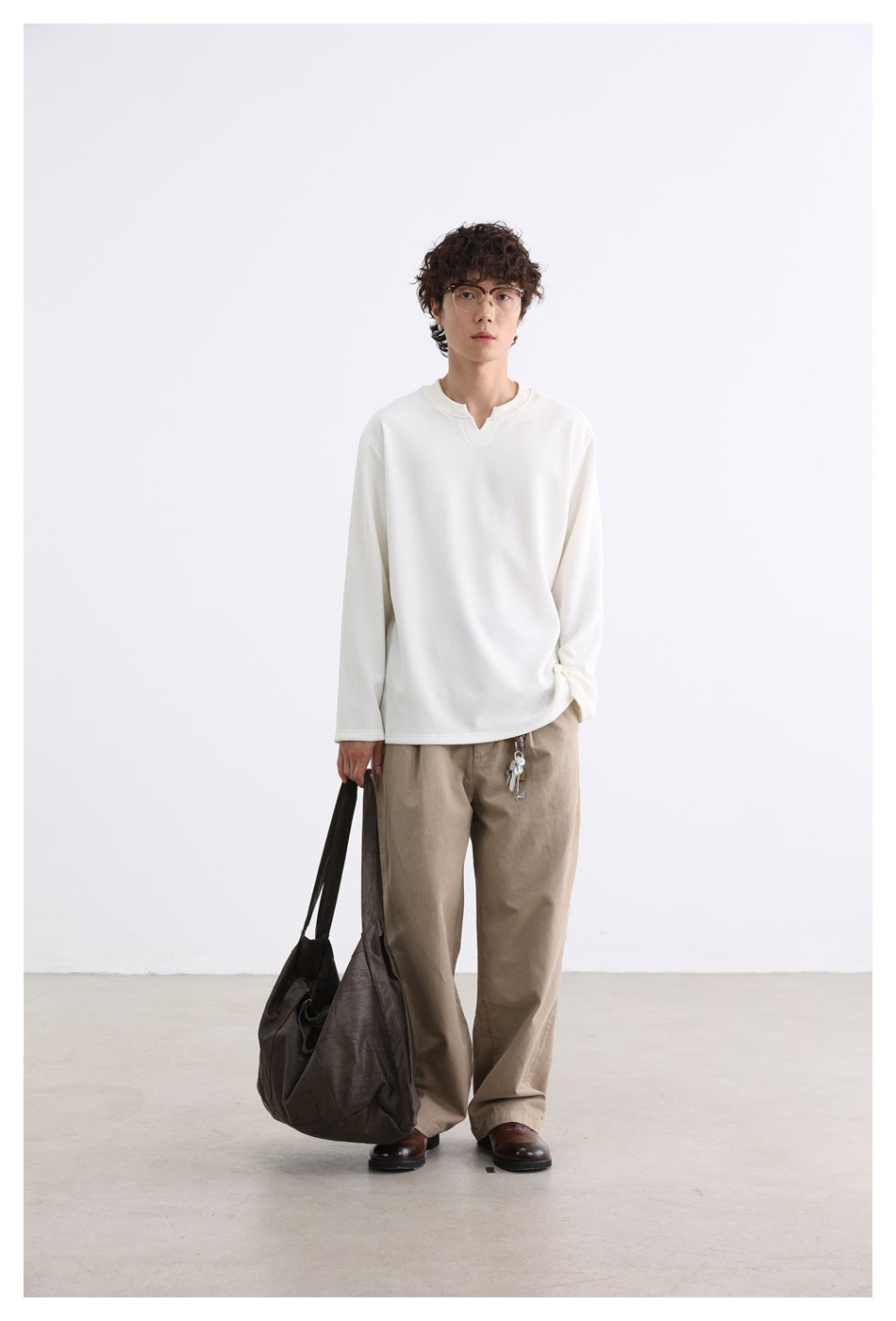 Full-length model wearing an ivory ribbed top and beige trousers, carrying a large dark shoulder bag.