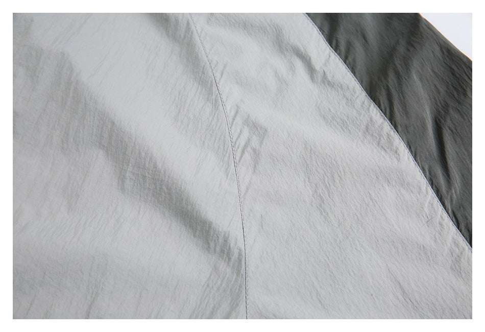 Close-up of curved stitching on a light gray jacket beside a dark contrasting panel.