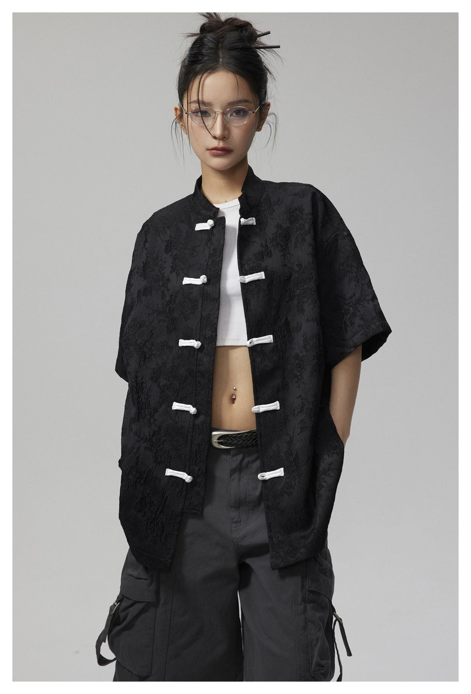 Front view of a model wearing a black textured short-sleeve jacket with white frog closures.