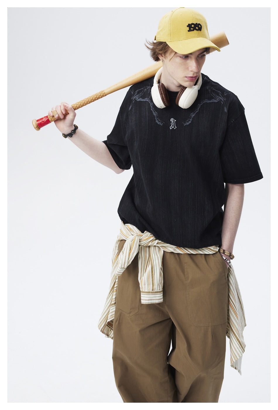 Close view of an oversized black T-shirt with dark shoulder graphics and a small embroidered chest letter, worn with olive