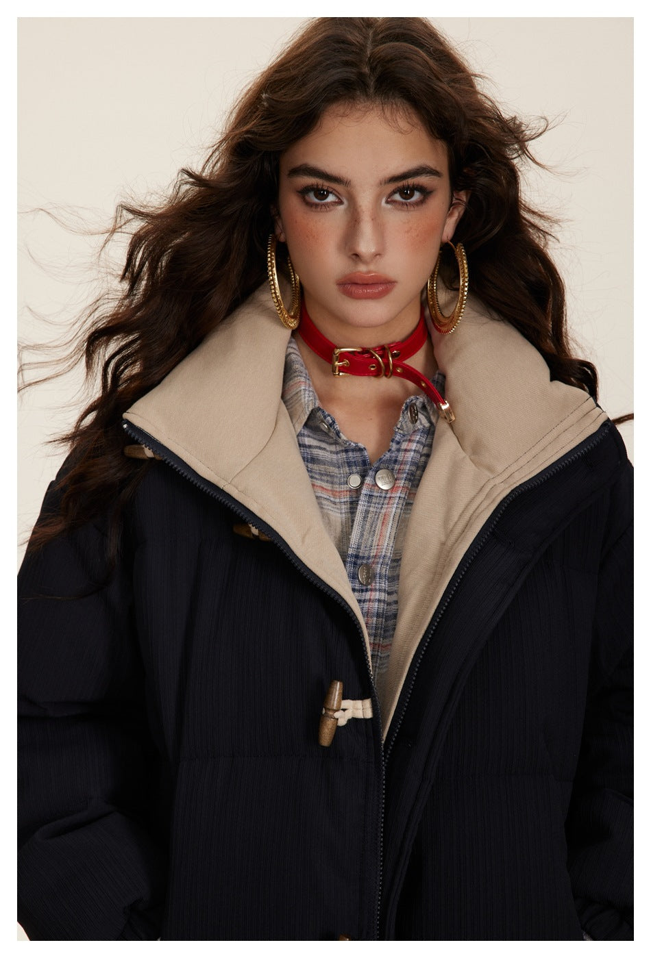 Close view of a model wearing a dark jacket with a beige collar, toggle closure and plaid shirt underneath.