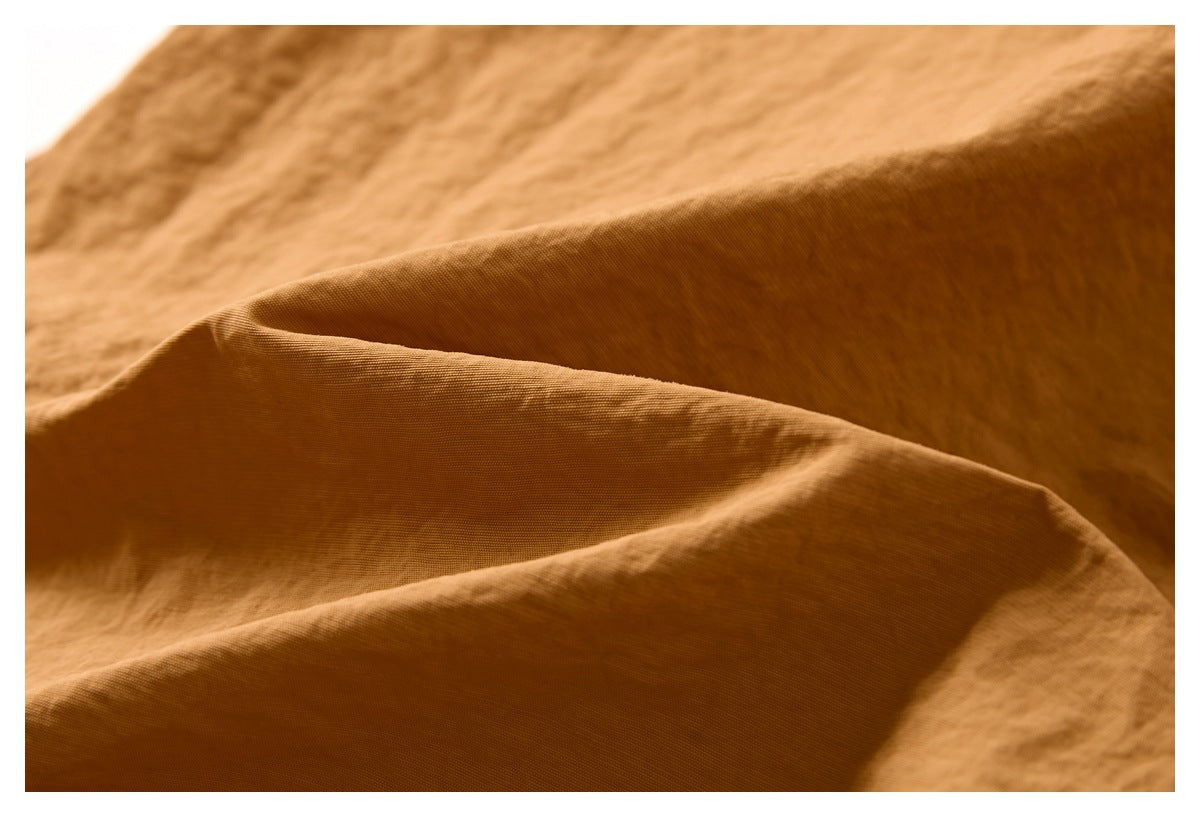 Macro view of the camel-brown shorts fabric, showing its fine weave and softly wrinkled texture.