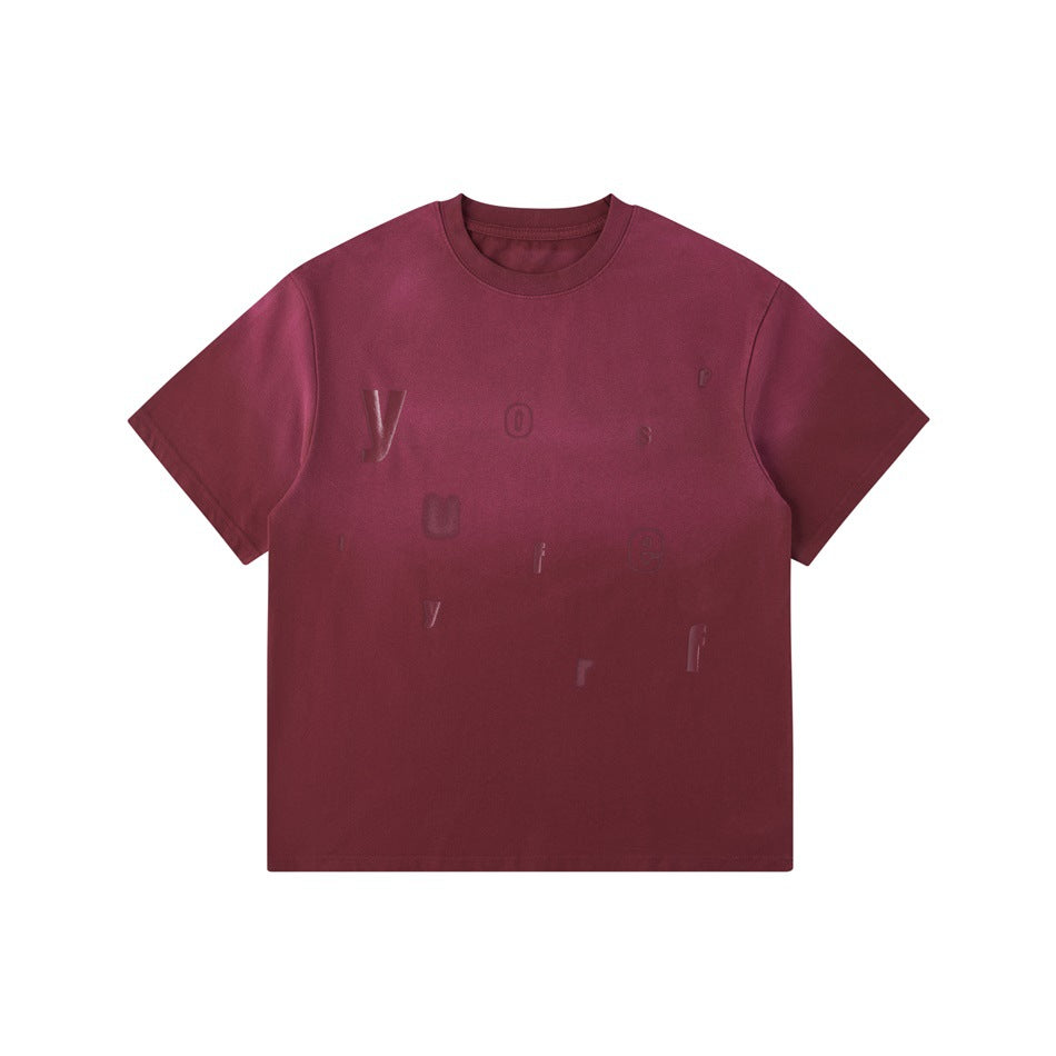 Burgundy red washed gradient crew-neck T-shirt with scattered tonal raised letters on the front, flat lay