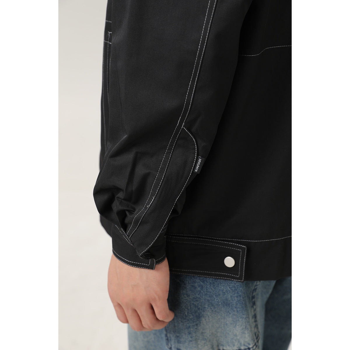 Close-up of the black jacket's contrast-stitched sleeve, cuff, and snap-button hem tab.