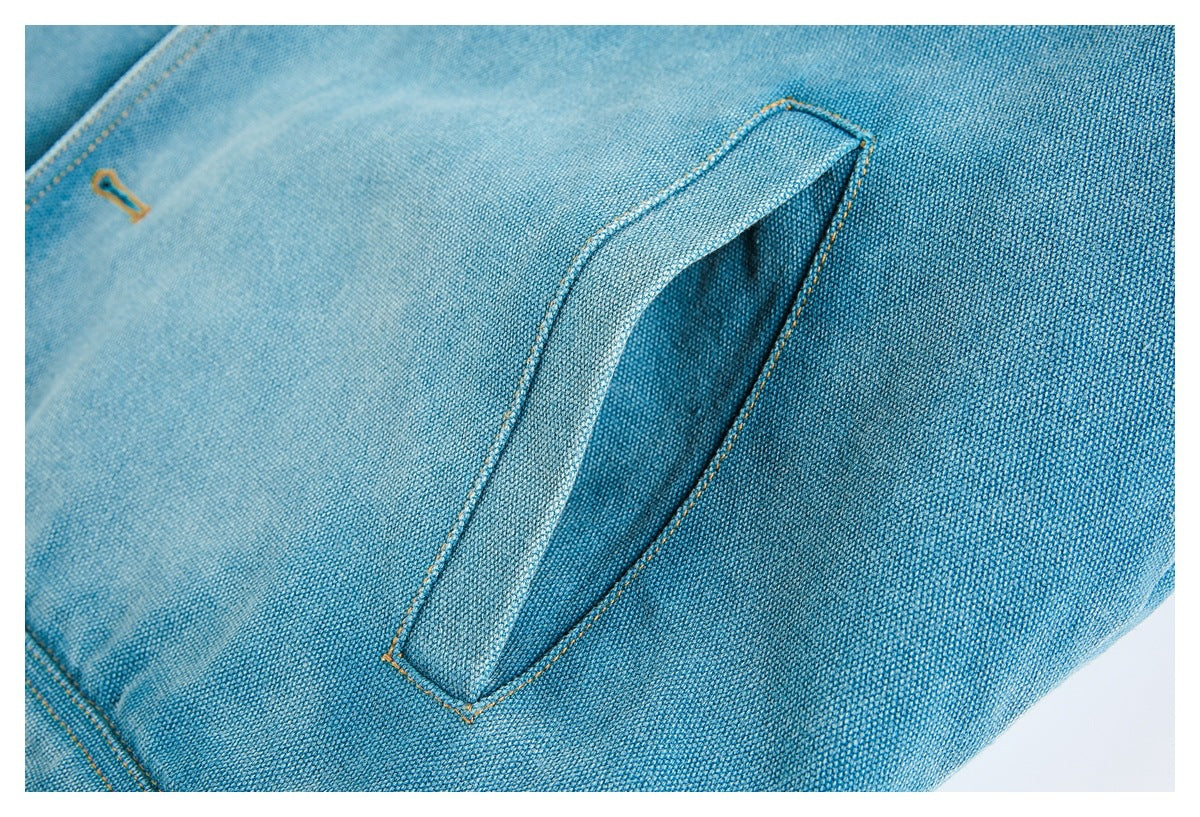 Close-up of a slanted welt pocket on blue woven fabric with ochre stitching.