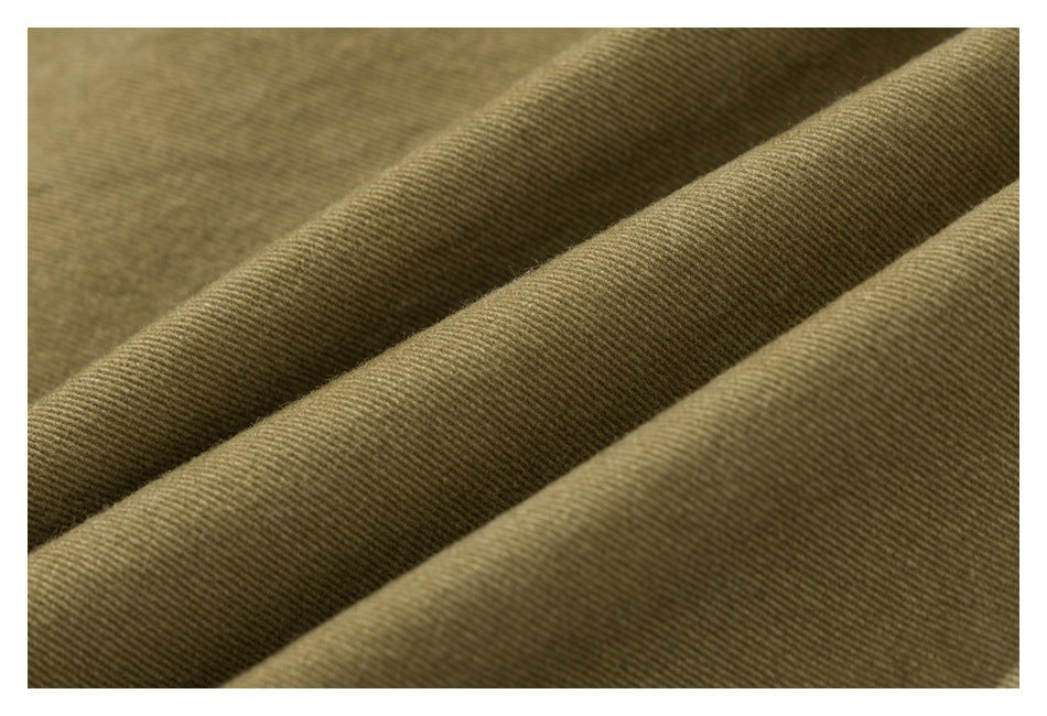 Close-up of olive-khaki fabric folded into soft ridges, showing a fine diagonal weave.