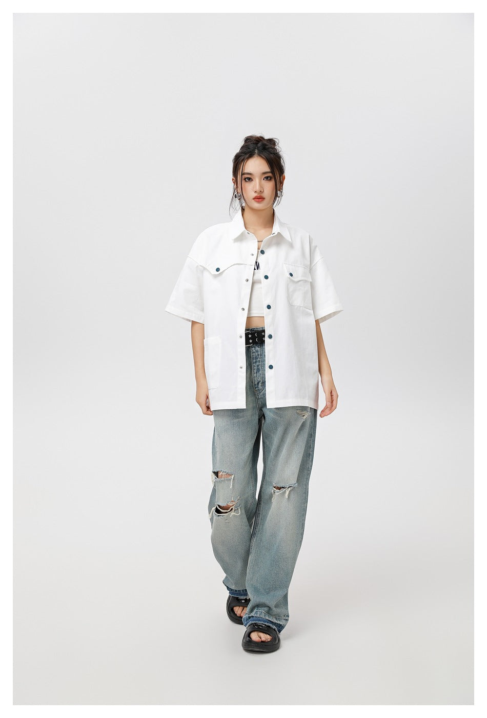 Full-length view of model in white short-sleeve snap-front shirt worn open over a white top with ripped jeans