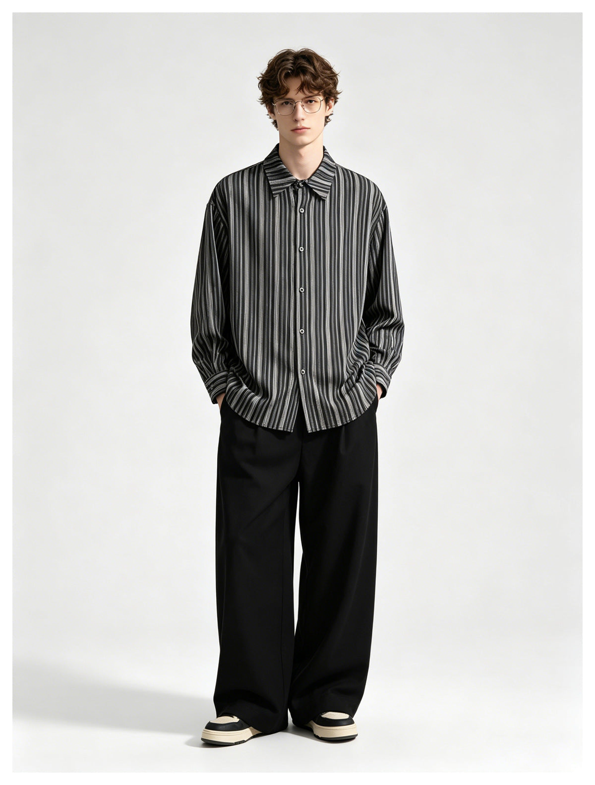 Model facing front in an oversized black and gray striped button-up shirt, wide black trousers and sneakers