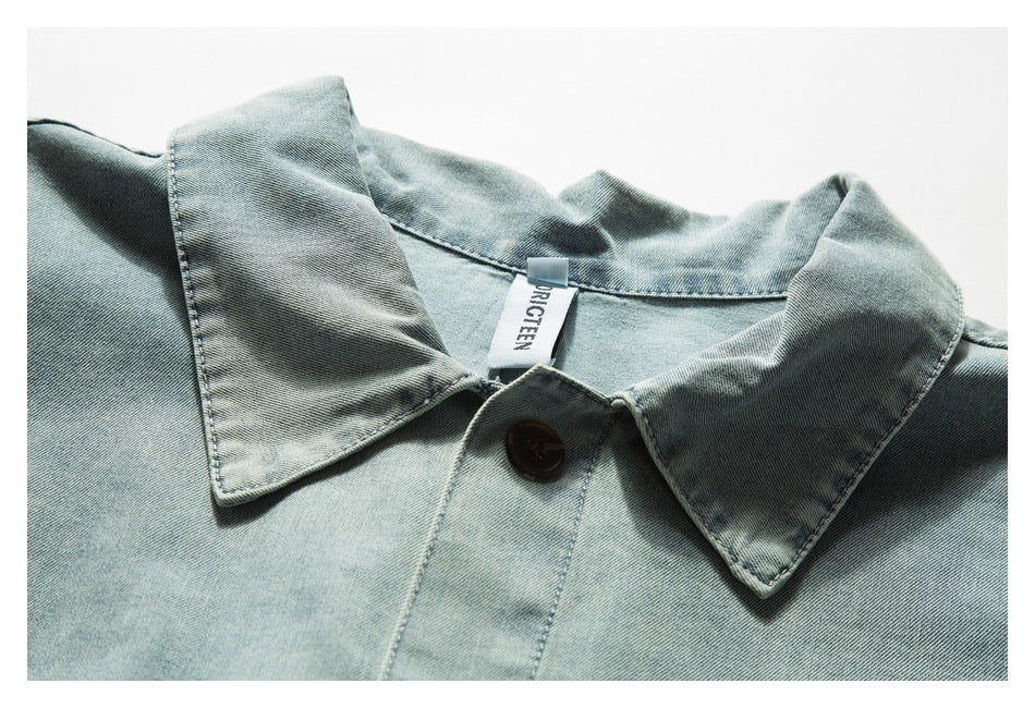 Close-up of a light blue denim shirt collar, dark button and sewn-in white neck label.