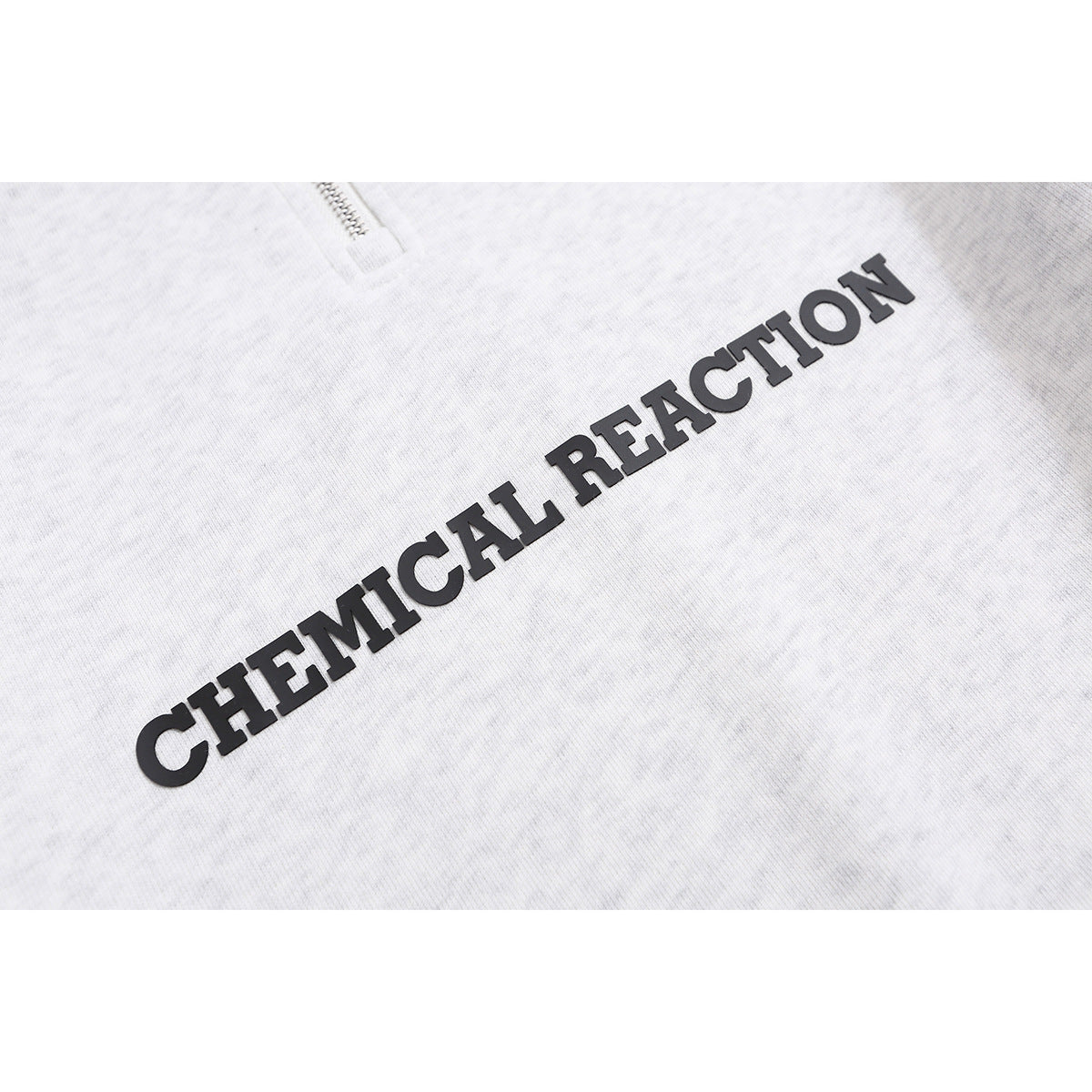 Close-up of raised black “CHEMICAL REACTION” lettering on the chest of a light gray hoodie.