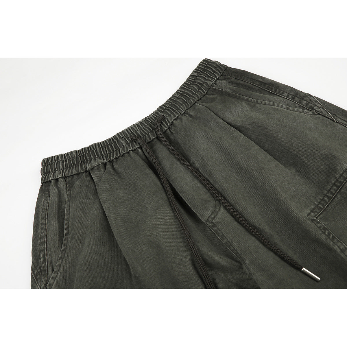 Close-up of dark olive wide-leg trousers showing an elastic waistband, drawstring, and front pocket seams.
