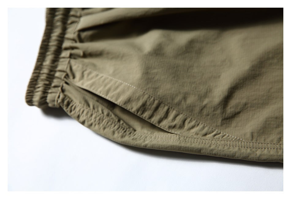 Close-up of an elastic waistband and stitched side opening on olive-khaki shorts.