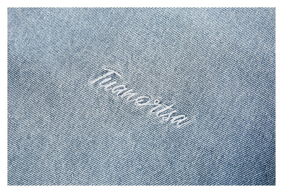 Close-up of white embroidered lettering on light blue denim; the text is not clearly legible.