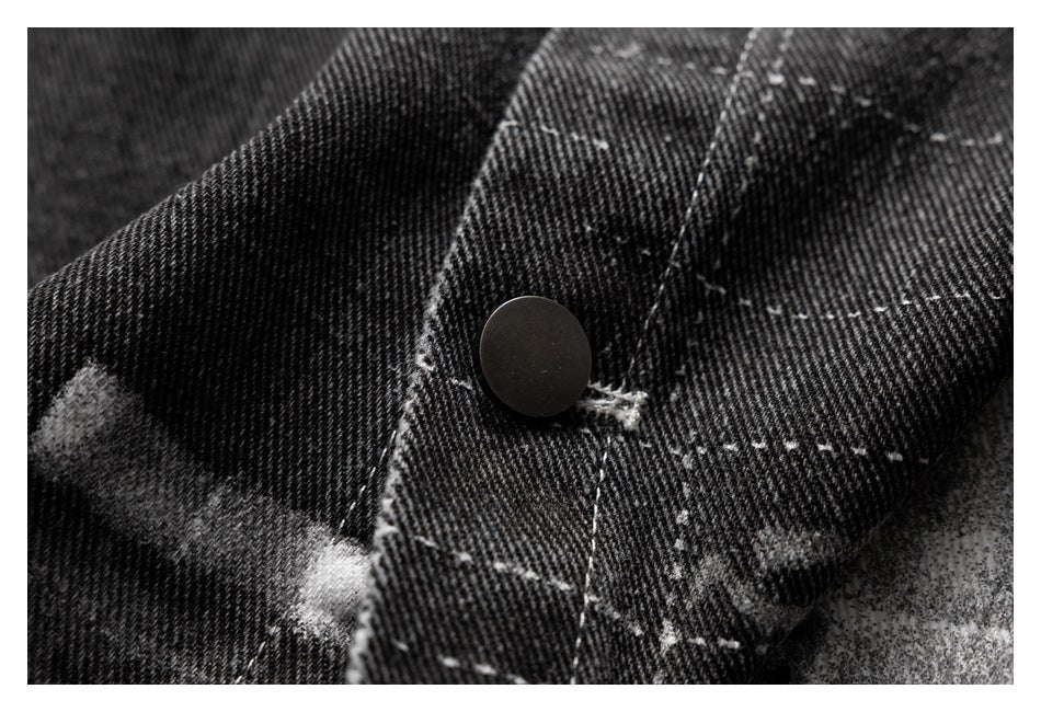 Close-up of a black-and-gray abstract-print garment with a dark snap button and white stitching.