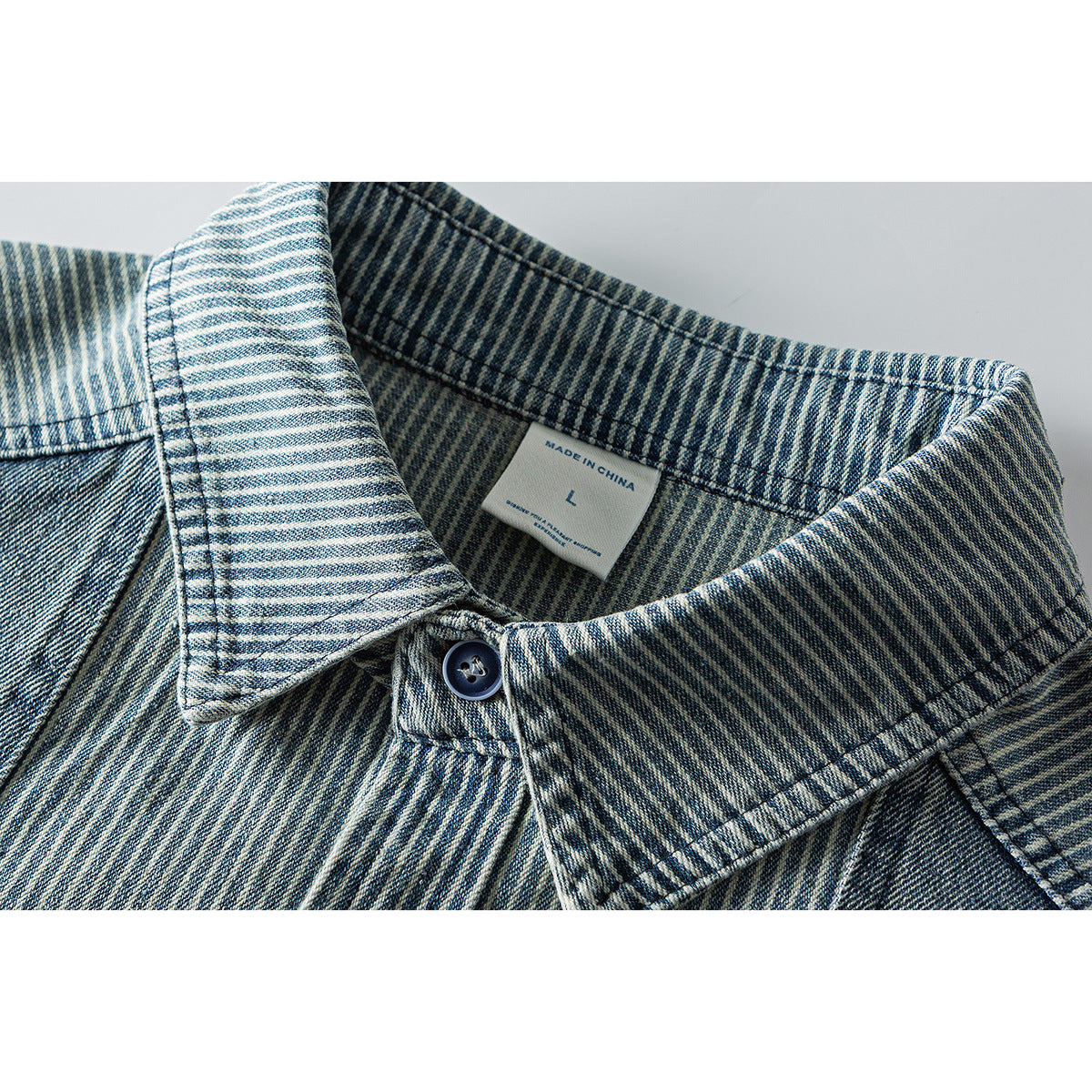 Close-up of a blue striped shirt collar, dark button, and inner size label.